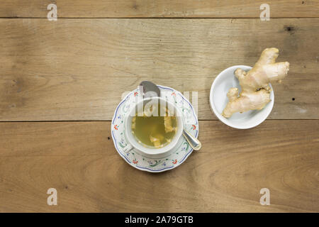 Hot tè allo zenzero in ceramica tazzina con materie di radice di zenzero fresco zenzero rizoma sul tavolo di legno sfondo, concetto di bibita salutare Foto Stock