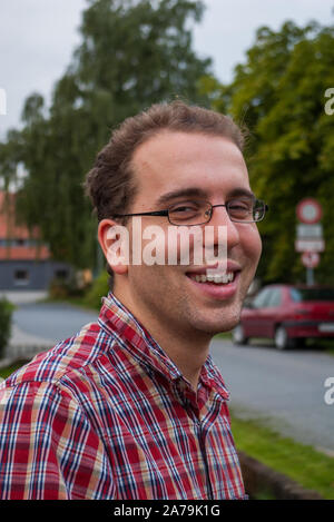 Bel giovane uomo caucasico con gli occhiali a sorridere all'aperto nei pressi di un segno di traffico in Germania Foto Stock