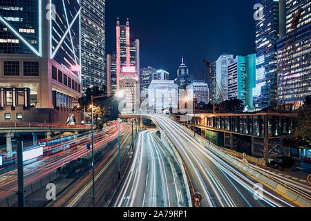 Occupato il traffico nella città moderna. Sentieri di luce di vetture contro notte urban skyline di Hong Kong. Foto Stock