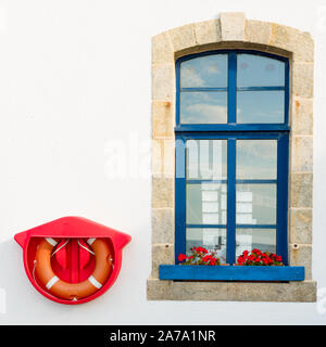 Una finestra di pietra con il blu e il rosso brillante anello di salvataggio montata su una parete bianca Foto Stock