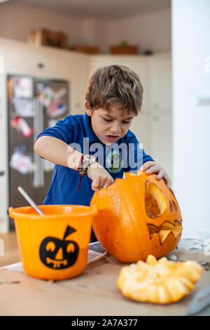 Ragazzo di 6 anni che raschia la cotenna all'interno di una zucca scolpita davanti a Halloween, Inghilterra, Regno Unito Foto Stock