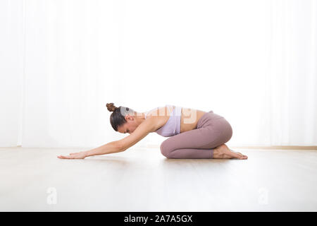 Ritratto di splendida sportiva attiva giovane donna a praticare yoga in studio. Bella ragazza pratica Ardha Kurmasana, mezza tartaruga pongono yoga. Un sano Foto Stock