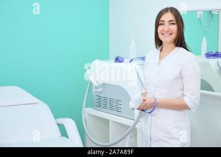 Sorridente medico in camice bianco in un salone di bellezza di depilazione laser e guardando la telecamera, copyspace Foto Stock