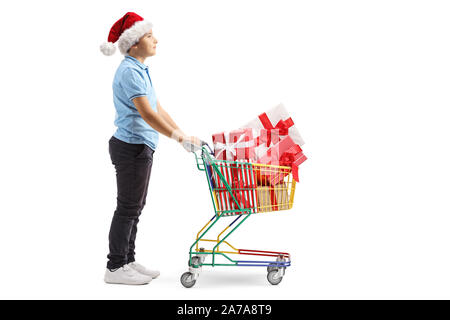 Lunghezza piena ripresa di profilo di un ragazzo con un Santa Claus hat spingendo un mini carrello con presenta isolato su sfondo bianco Foto Stock