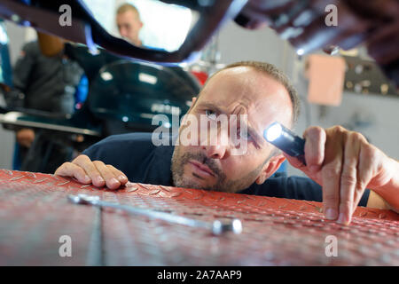 Lavoro meccanico sul lato inferiore di una vettura di elevate Foto Stock