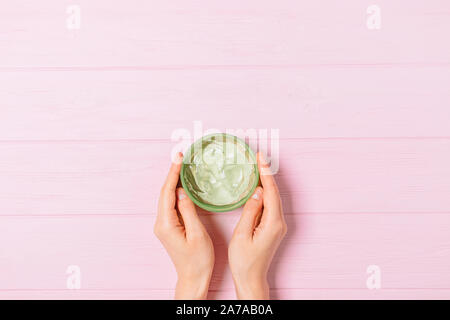 Donna di mani tenendo aperto il vaso di verde aloe vera gel sulla tabella di rosa, minima piana composizione laici. Foto Stock