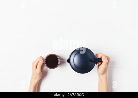 Geyser macchinetta per il caffè e la tazza di caffè appena macinato in mani femminili su bianco tavolo in legno con copia spazio, vista dall'alto Foto Stock