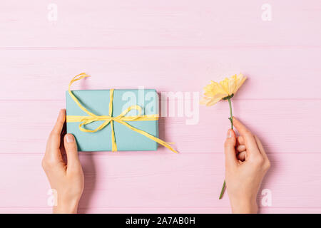 Mani femminili azienda confezione regalo e fiori freschi su sfondo rosa e colorati di festosa molla piatta disposizione laici. Foto Stock