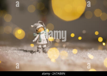 Decorazione di Natale figurine a tema. Statuetta boy in maglia cappelli e sciarpe. Decorazione per albero di Natale. Decorazioni festive, calde luci bokeh di fondo Foto Stock