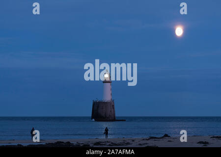 Fotografi sulla spiaggia di Rattray testa, sull'Aberdeenshire Costa, fotografare la luna che sorge dietro il faro al tramonto Foto Stock