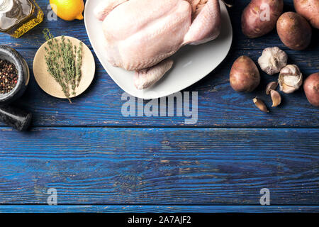 Il pollo crudo in una piastra bianca su sfondo blu sullo sfondo di legno con limone e un rametto di timo e vari ingredienti, laici piatta Foto Stock