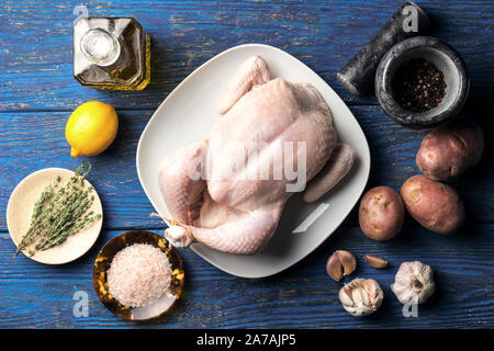 Il pollo crudo in una piastra bianca su sfondo blu sullo sfondo di legno con limone e un rametto di timo e vari ingredienti, laici piatta Foto Stock