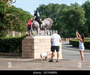 Bambini aventi foto scattate con il cellulare mentre a cavallo di lion statua nei giardini italiani il Parco Stanley Blackpool Lancashire England Regno Unito Foto Stock