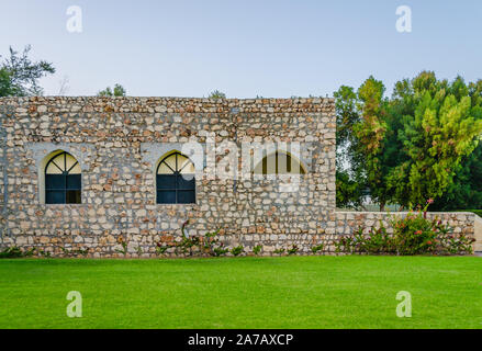 Vecchia casa in pietra con finestra nera archi circondato da piante e da un prato verde nella parte anteriore. Da Muscat Oman. Foto Stock