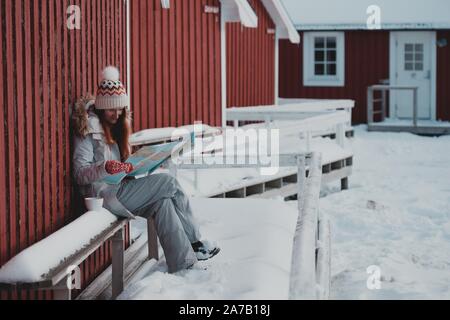 Ragazza turistica si siede vicino rorbu con una mappa a isole Lofoten. Norvegia Foto Stock