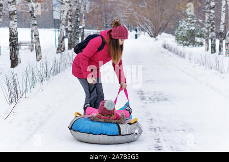 Attivo giovane madre rotoli il suo bambino su un snow tubing. Attività invernali. La Felicità di essere un genitore. Aspetto familiare. Foto Stock