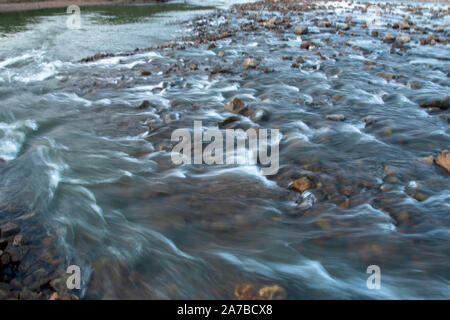 Gettare acqua di un fiume con il riflesso del cielo blu prese con una lenta velocità di otturatore. Foto Stock