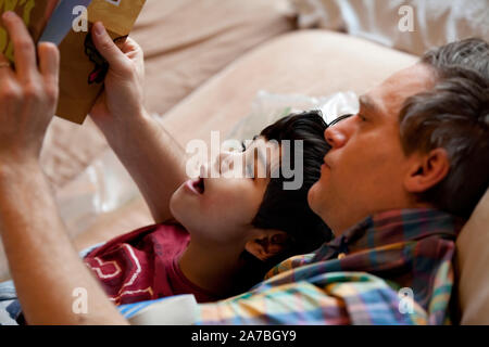 Otto anni che biracial ragazzo lettura libro con padre caucasica mentre giaceva a letto Foto Stock