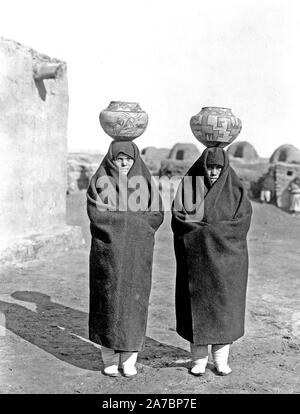 Due femmine, a lunghezza piena, indossando coperte, pentole su capi Foto Stock