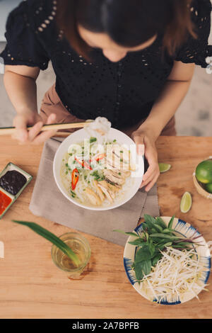 Pho vietnamita noodle soup. Carni bovine con peperoncino, basilico, Riso tagliatelle, germogli di fagioli che mostra tagliatelle prelevato con bacchette Foto Stock