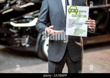 Elegante consulente di vendita che mostra un disegno sul tema della eco-friendly di auto elettriche, vendita di veicoli presso la concessionaria auto Foto Stock