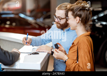 Coppia giovane firma alcuni documenti, l'acquisto di una nuova auto nel moderno showroom della concessionaria auto Foto Stock