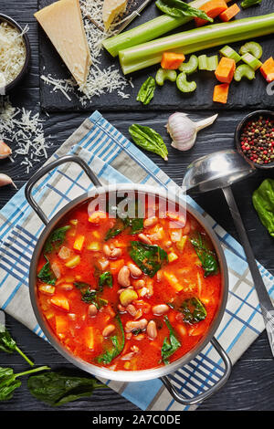 Fagioli borlotti minestra con spinaci e parmigiano Pomodori in pentola di metallo su un tavoli in legno nero, verticale vista da sopra Foto Stock