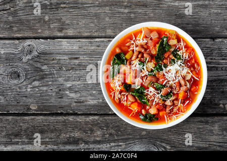 Italiano o borlotti cranberry zuppa di fagioli con sedano, verdure, spinaci, il parmigiano e i pomodori in una ciotola bianco su una tavola in legno rustico, orizzontale Foto Stock