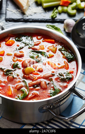 Close-up di italiano o borlotti cranberry zuppa di fagioli con sedano, verdure, spinaci, il parmigiano e i pomodori in una pentola di metallo su un nero scheda in legno Foto Stock