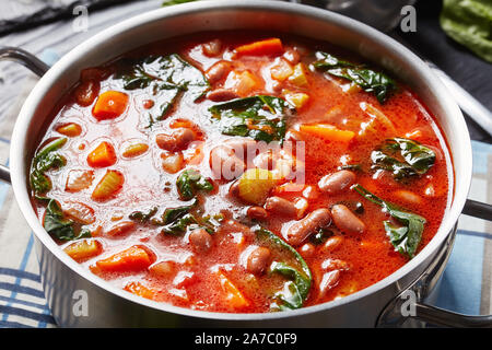 Close-up di italiano o borlotti cranberry zuppa di fagioli con sedano, verdure, spinaci, il parmigiano e i pomodori in una pentola di metallo su un nero scheda in legno Foto Stock