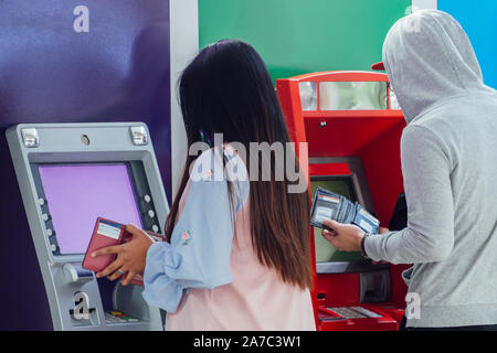 Giovani asiatici l uomo e la donna sono holding wallet e premendo il perno numero di protezione di ritirare denaro contante dalla carta di credito alla banca ATM macchina per il negozio Foto Stock