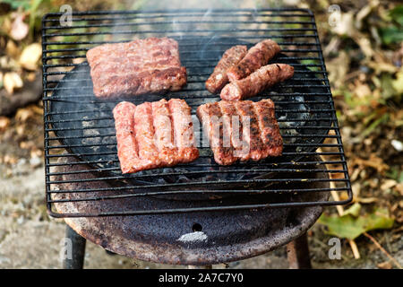 Cucina balcanica Cevapi di maiale e grigliate di carni macinate, sulla griglia improvvisata Foto Stock