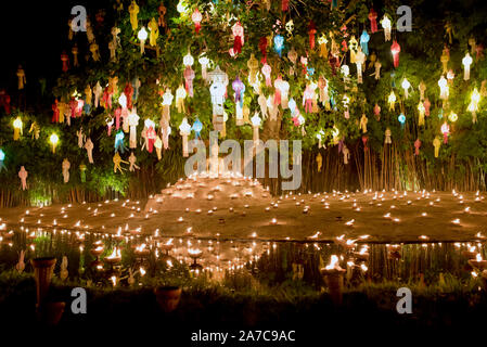 I monaci in abiti dello zafferano seduto sotto agli alberi illuminata con centinaia di lanterne in preghiera, Chiang Mai, Thailandia Foto Stock