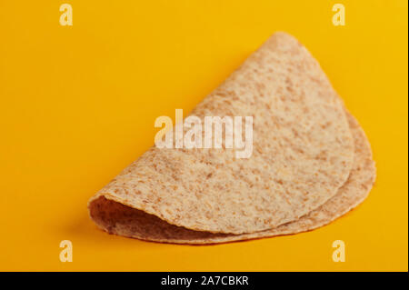 Uno vuoto tortilla ripiegata isolato su sfondo giallo vista laterale Foto Stock