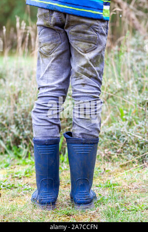 Ragazzo in piedi sul green indossando wellies blu. Foto Stock