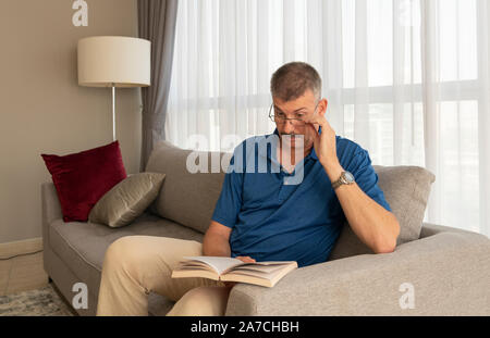 Uomo di mezza età sul suo divano la lettura di un libro Foto Stock
