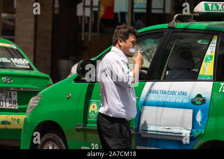 Il Vietnam, Nha Trang city, 25 marzo 2019 un vietnamita taxi driver nervosamente fuma in attesa al di fuori il suo verde taxi Foto Stock