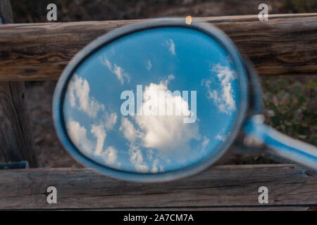 Close-up di uno specchio retrovisore di un motociclo con la riflessione in esso di un cielo blu con nuvole, libertà, viaggi, vagare Foto Stock