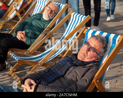 Prendere il sole in sedie a sdraio sul molo di Brighton Foto Stock