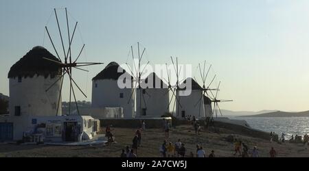 Mykonos, Grecia: iconico mulini a vento di Mykonos isola durante un tramonto dopo un'estate giornata soleggiata lungo il mare blu Foto Stock