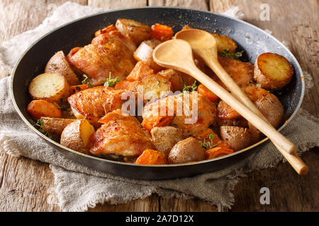 Cuocere le cosce di pollo con patate e carote close-up in una padella sul tavolo orizzontale. Foto Stock