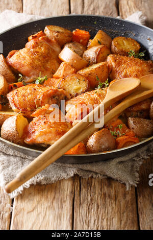 Stile rustico cosce di pollo al forno con patate, carote, timo in salsa di vino di close-up in una padella sulla tavola verticale. Foto Stock