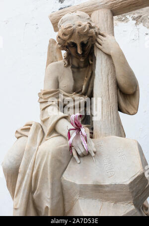 Fiore in mano della statua di donna holding croce nel cimitero. Foto Stock