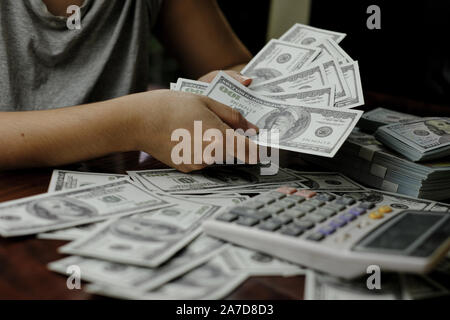 Mano azienda smartphone e calcolatrice su una pila di 100 dollari USA banconote un sacco di soldi Foto Stock