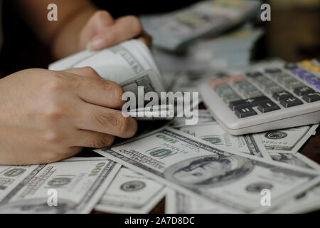 Mano azienda smartphone e calcolatrice su una pila di 100 dollari USA banconote un sacco di soldi Foto Stock