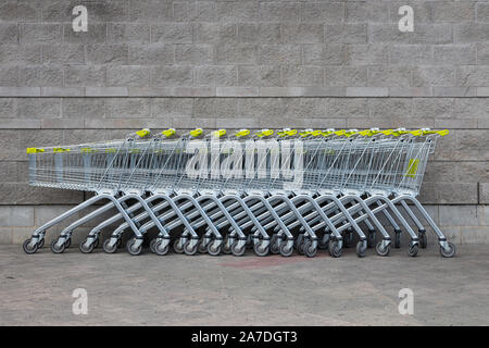 Carrelli con manico di colore giallo in piedi uno per uno nelle vicinanze di mattoni grigi di parete supermercato sfondo. Foto Stock