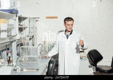 Scienziato maschio conduce esperimenti di chimica con fluidi nel laboratorio di analisi mediche Foto Stock