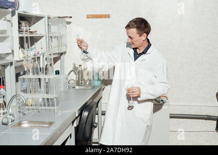 Scienziato maschio conduce esperimenti di chimica con fluidi nel laboratorio di analisi mediche Foto Stock