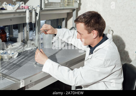 Scienziato maschio conduce esperimenti di chimica con fluidi nel laboratorio di analisi mediche Foto Stock