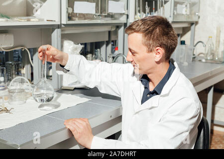 Scienziato maschio conduce esperimenti di chimica con fluidi nel laboratorio di analisi mediche Foto Stock